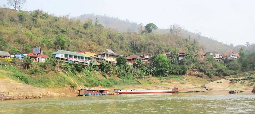 Riverside homes and boats beneath the green hills of Pak Beng